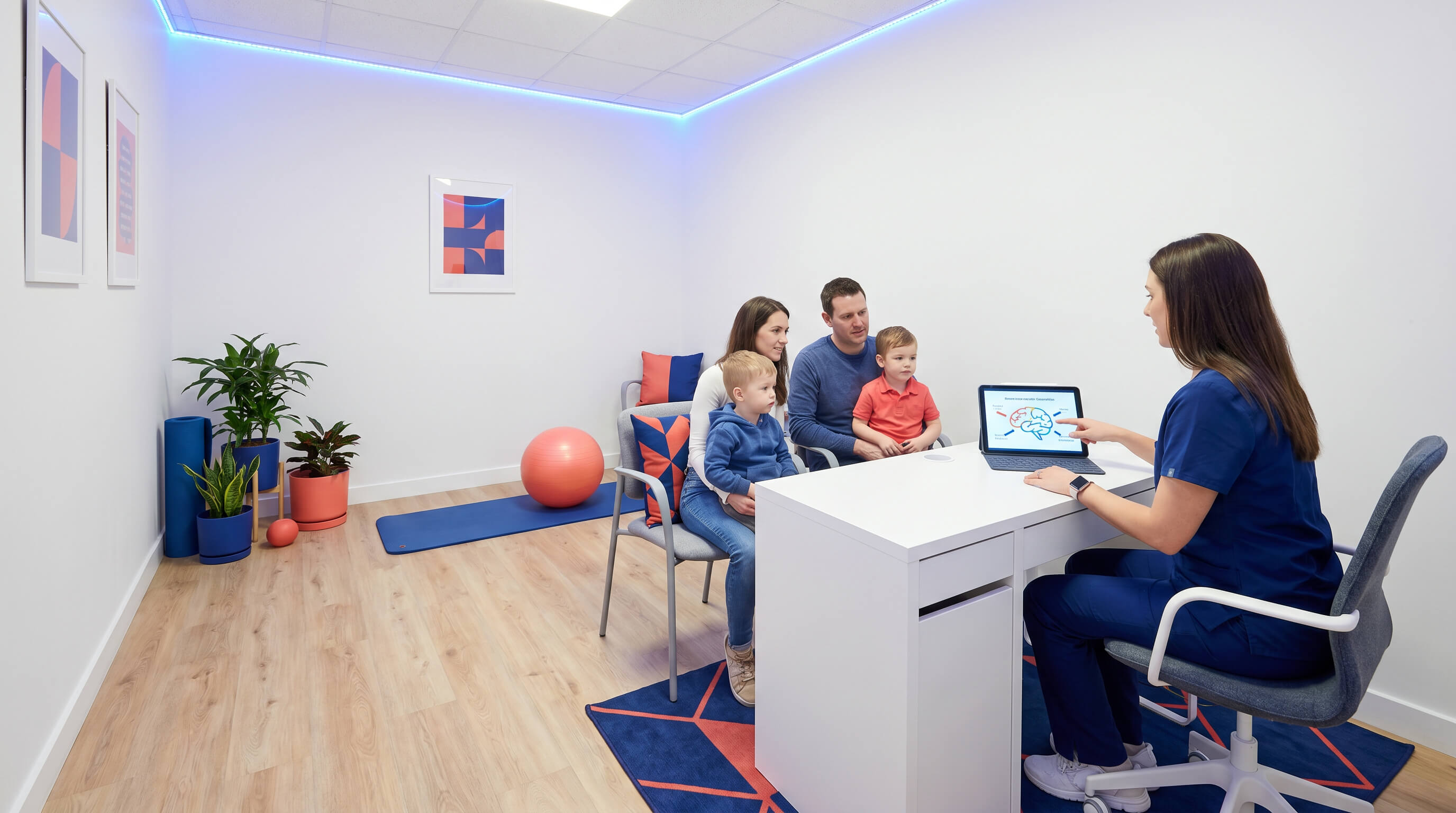 Eine Familie sitzt mit ihren zwei Kindern auf dem Schoss in einer Praxis. Ärztin sitzt an Ihrem Schreibtisch und zeigt Grafik eines Gehirns. 